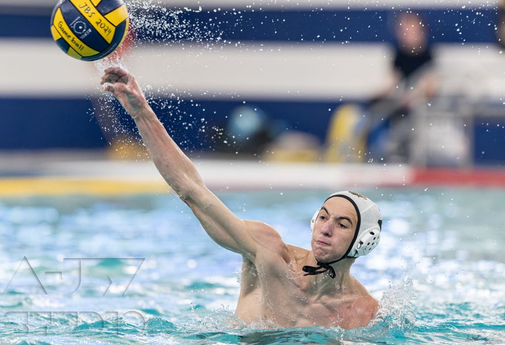 A water polo player reaches up to catch a yellow ball during a match.