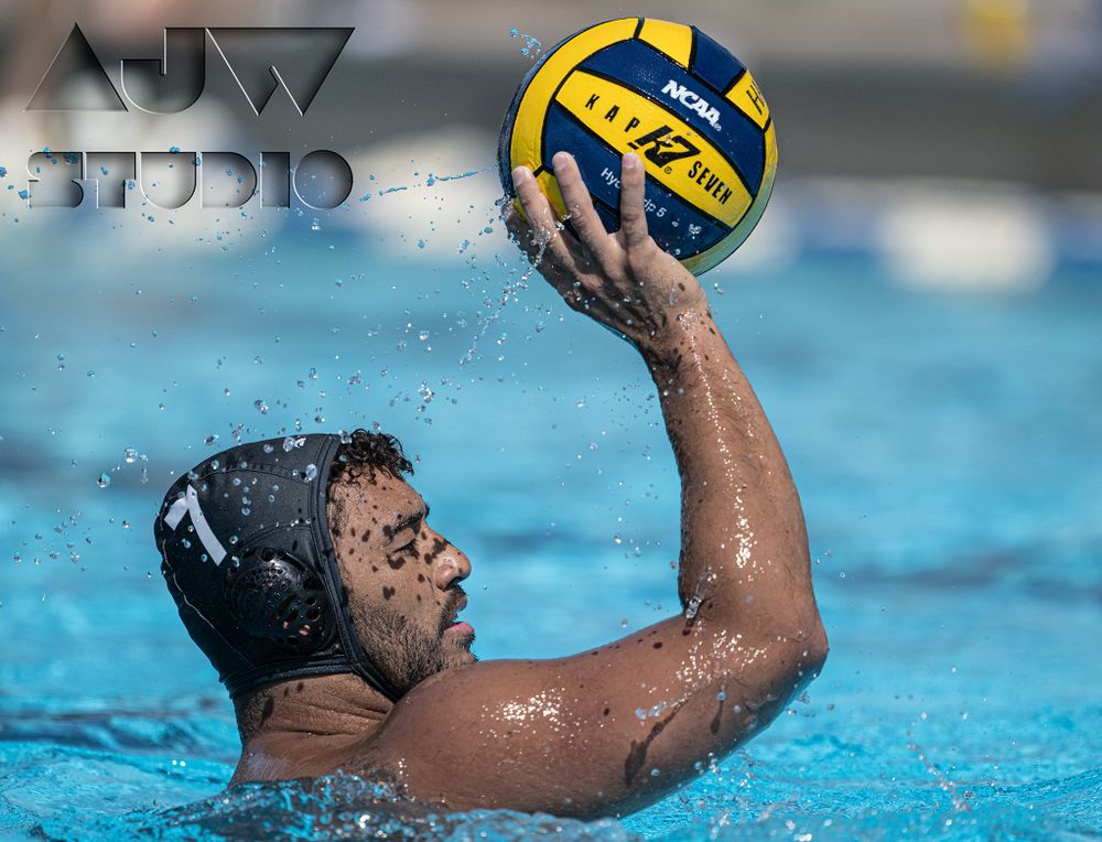 A water polo player in a cap holds up a yellow and blue ball in the pool.