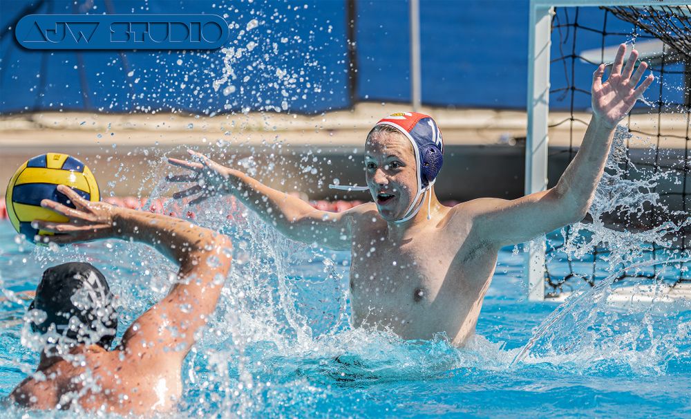 Athletes compete for the ball during an intense water polo match with splashing water.