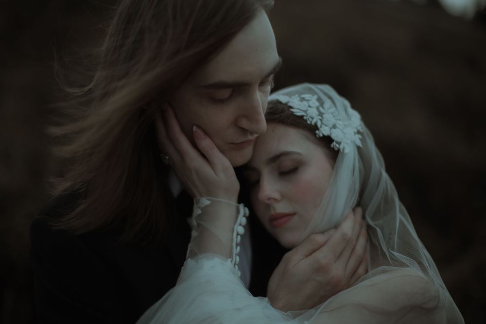 A groom tenderly cradles a bride in a veil during an intimate, moody wedding portrait.
