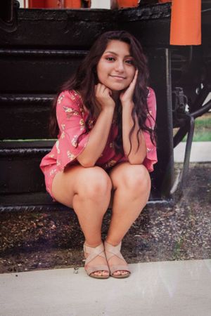 Casual portrait series in pink dress sitting near orange wall outdoors.
