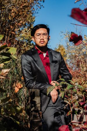 Stylish portrait session featuring formal attire with a black patterned suit and red tie in autumn scenery.