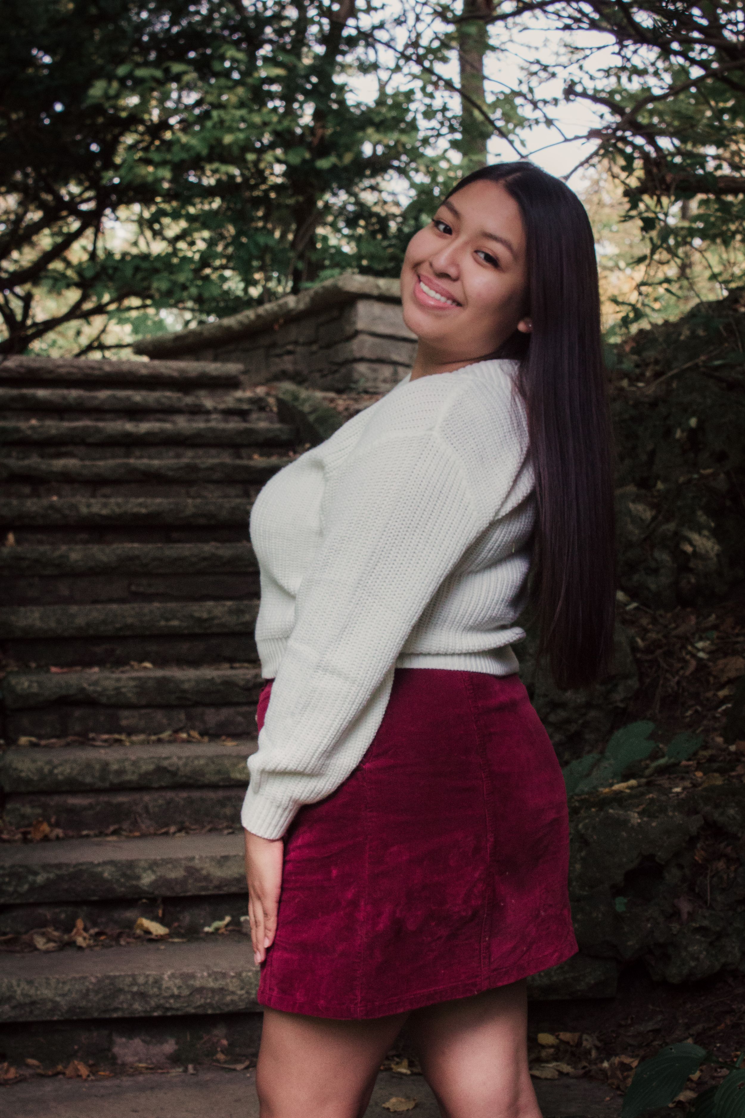 A casual portrait on stone steps wearing a white sweater and burgundy skirt.