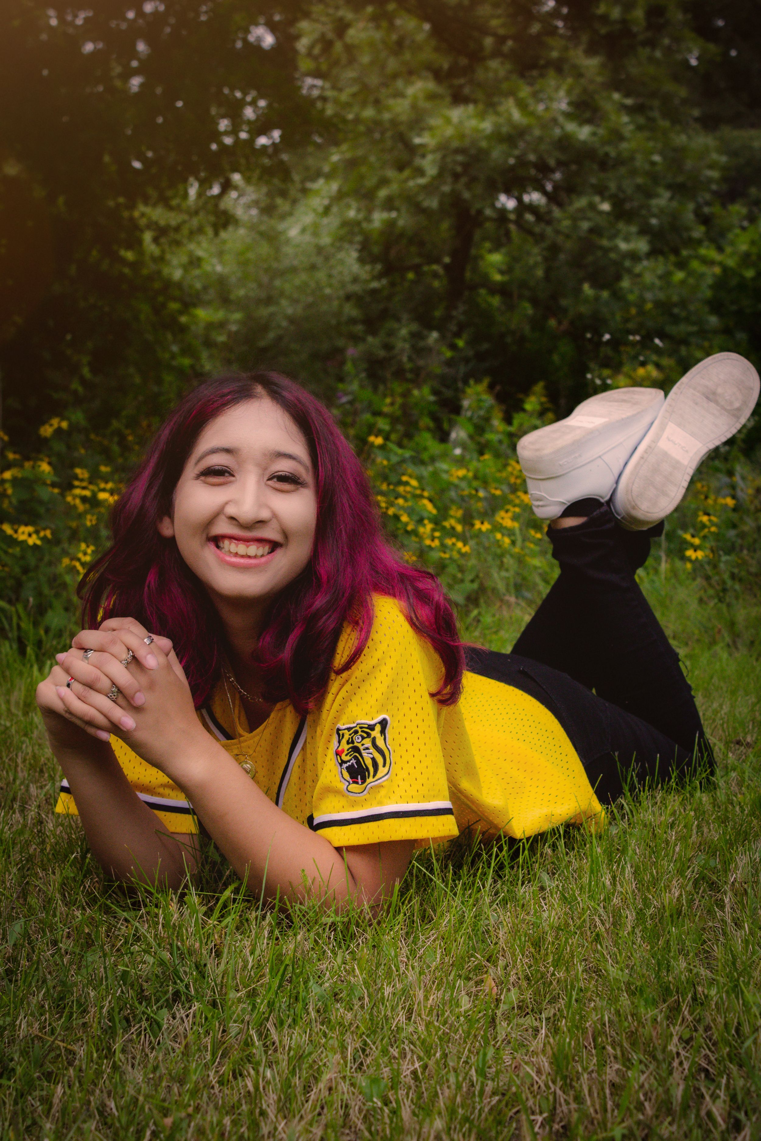 Person in yellow Hufflepuff jersey laying in grass with colorful purple hair on a sunny day.