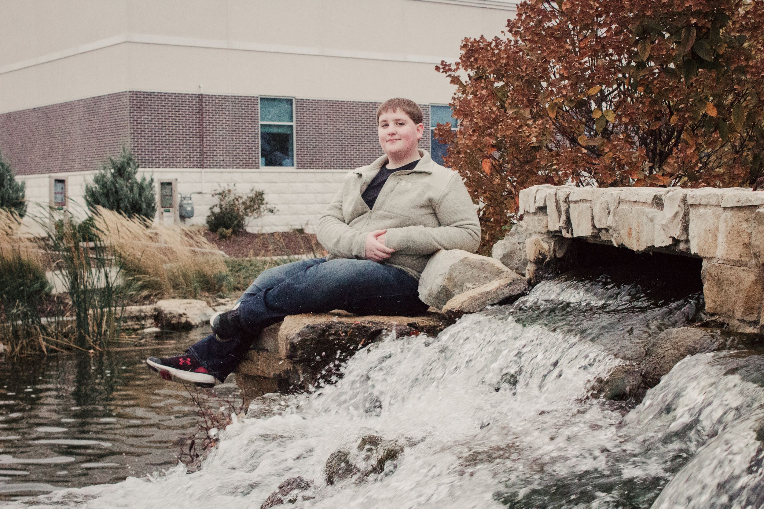 A person relaxes by a small waterfall on stone landscaping during autumn.