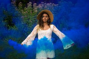 A bohemian style portrait with a lace dress and straw hat against a vivid blue background.