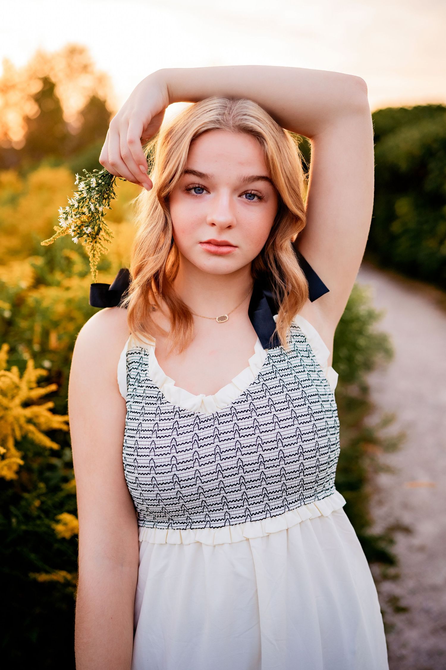 Young ballet dancer in a white summer dress poses during golden hour sunset.