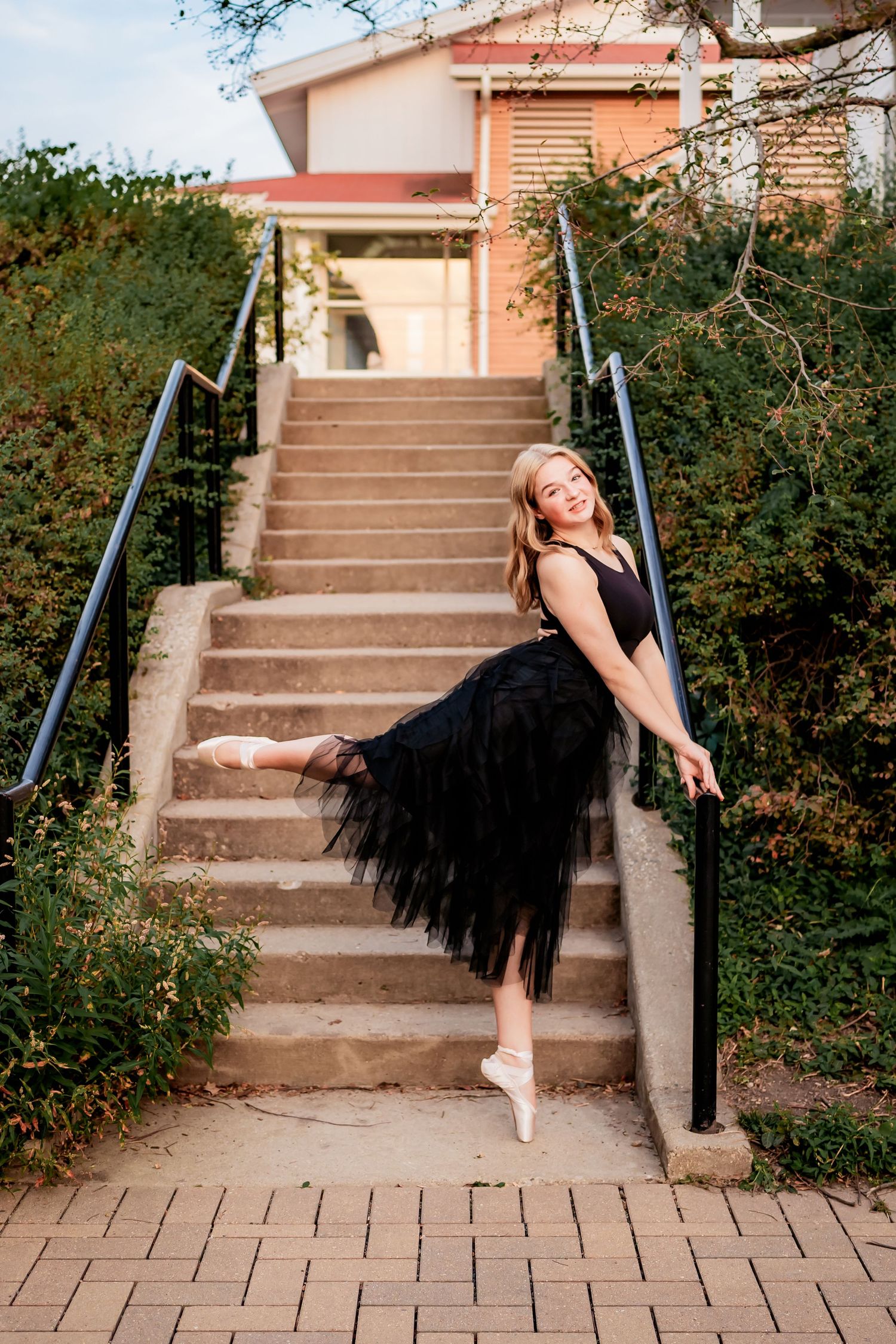 Dancer in black tutu strikes elegant pose on outdoor staircase.
