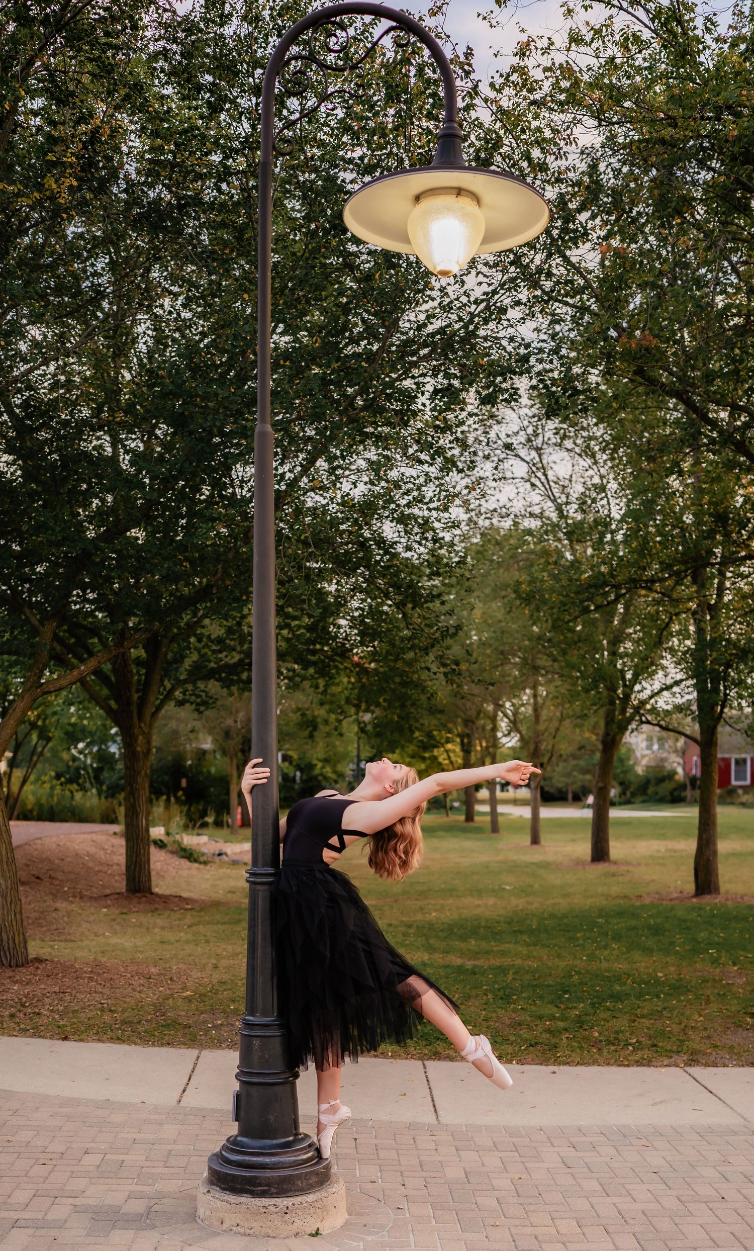 Dancer strikes dramatic pose against vintage lamppost at dusk.