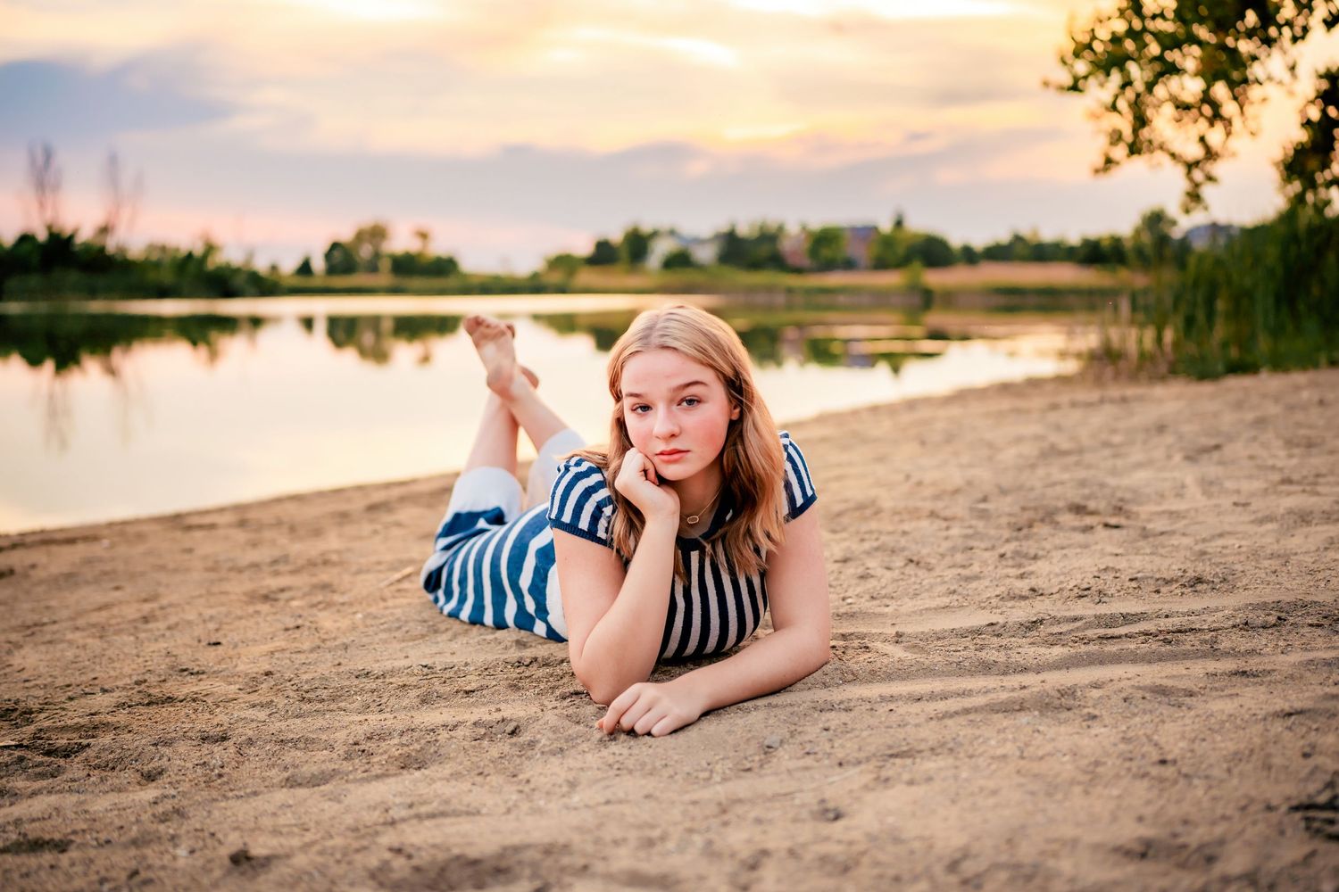 Person in striped outfit relaxes on sandy beach at sunset.