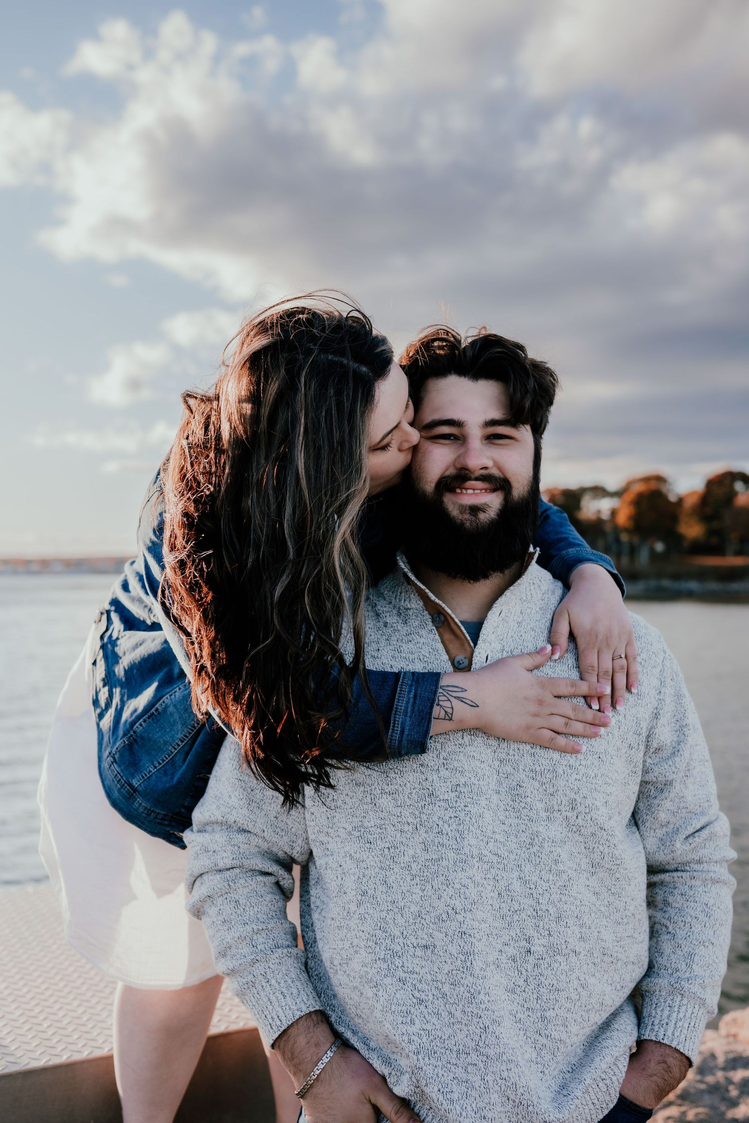 A romantic couple sharing intimate moments on a beach at sunset with dramatic cloudy skies in the background.