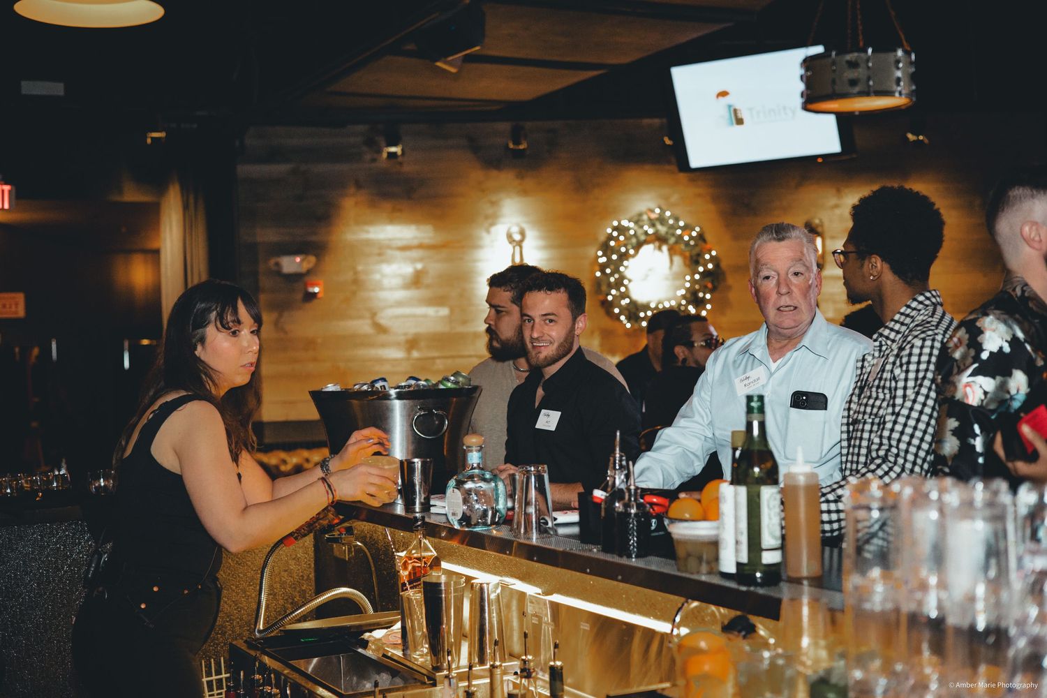 Dimly lit bar interior with customers seated along wooden counter.