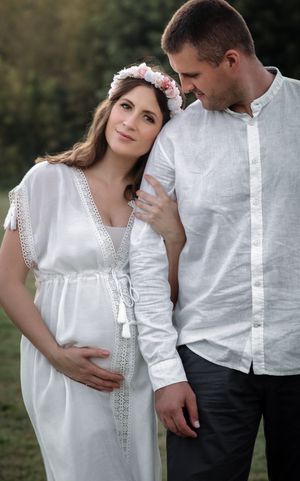 pregnant women leaning on her husband in white dress touching her belly on their maternity photoshoot