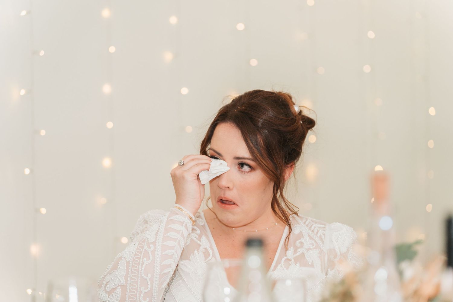 Emotional moment captured at a wedding with soft twinkling lights in the background while wiping away tears.