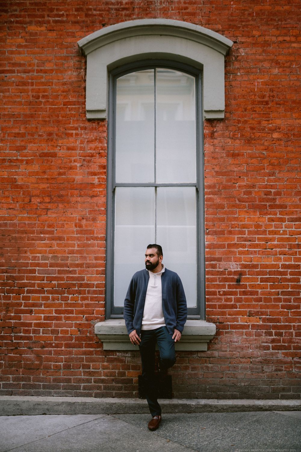 Contemporary portrait against red brick wall with tall white window frame in urban setting.