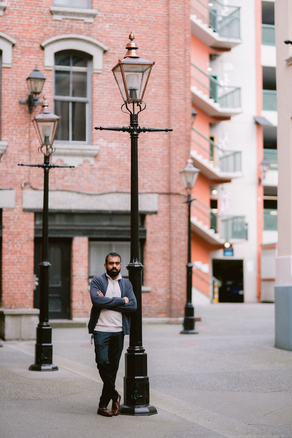Person standing next to vintage lamp post against brick building in urban setting.