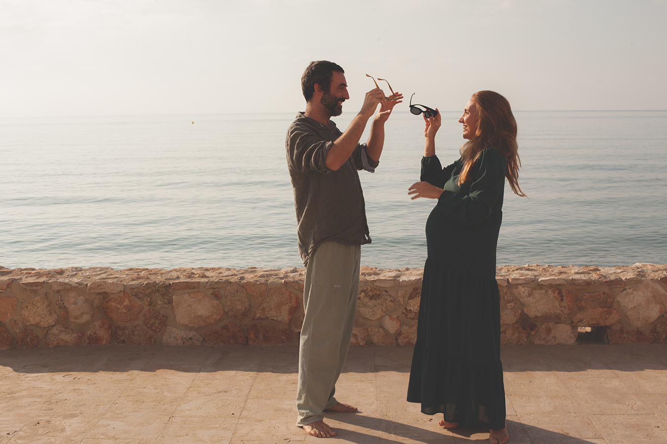 coppia,uomo e donna felici, donna incinta, scambio occhiali da sole, sessione fotografica Maternity al mare, donna e uom Altafulla in Spagna