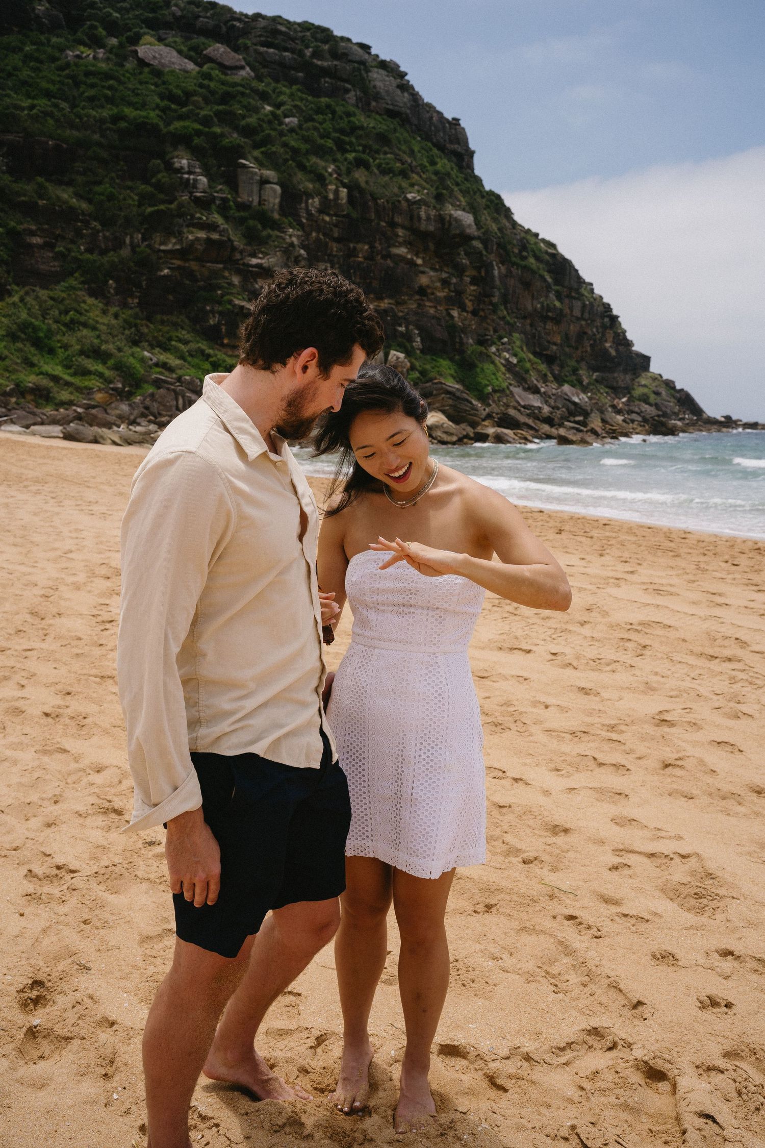 A joyful couple sharing a moment together on a scenic beach with rocky cliffs.