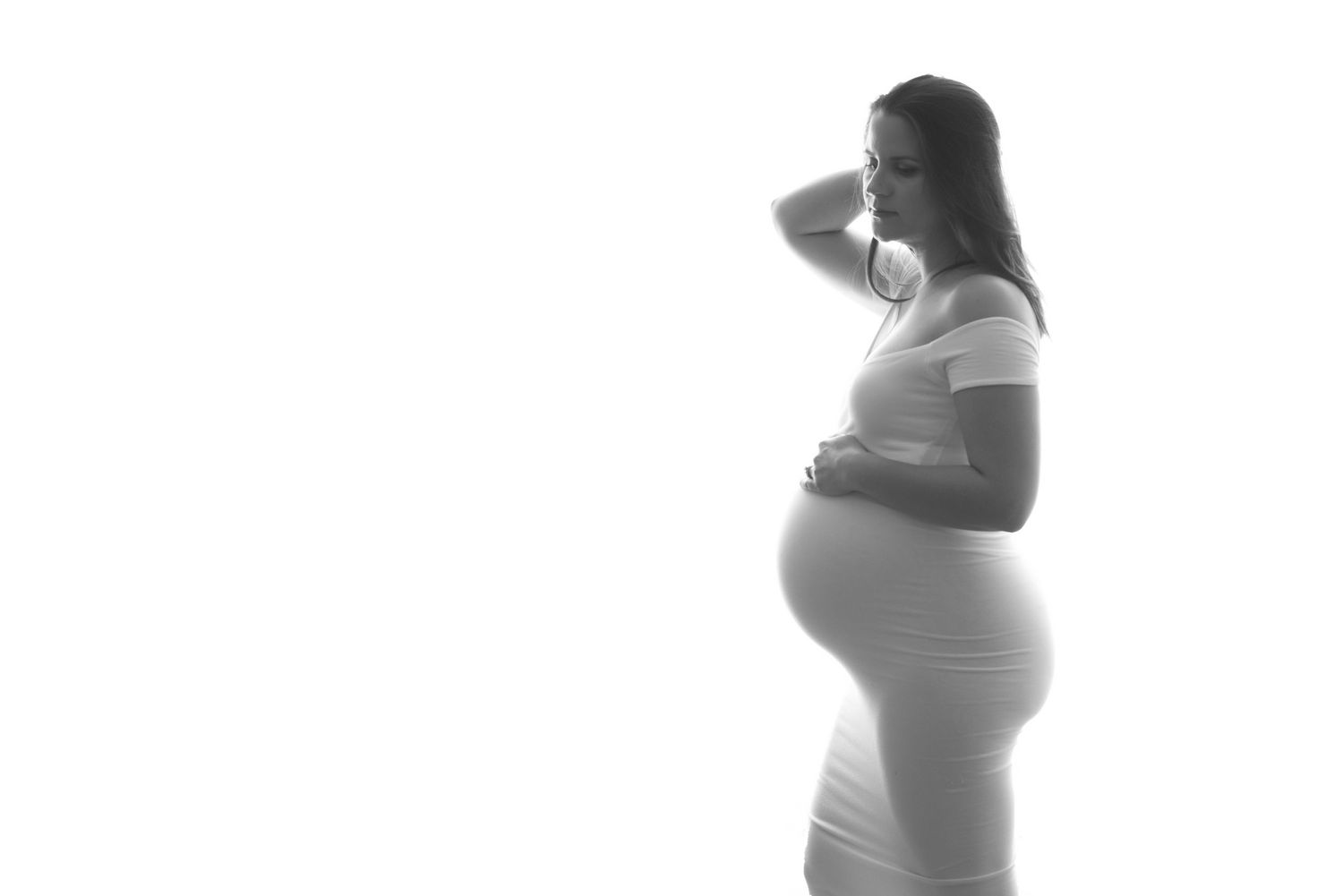 A black and white silhouette of an expectant mother in profile wearing a fitted outfit that accentuates her baby bump.  Fresno Maternity Pho