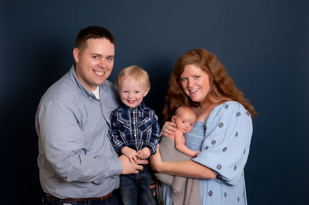 Studio portrait of a family of four in coordinated navy and gray outfits against a dark background.