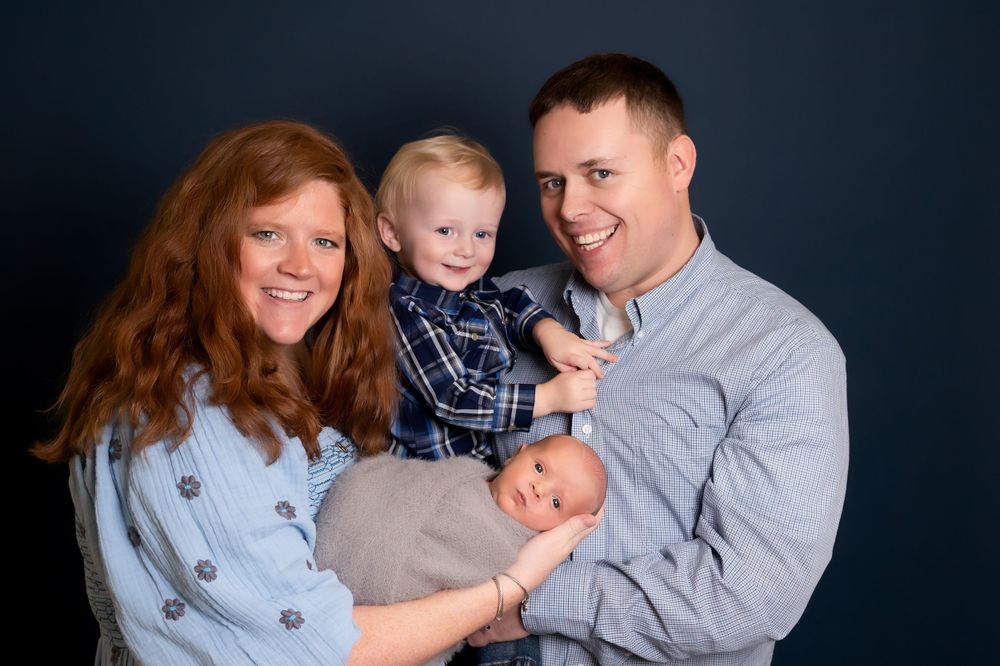 Studio portrait of a family of four in coordinating blue outfits against a dark background.
