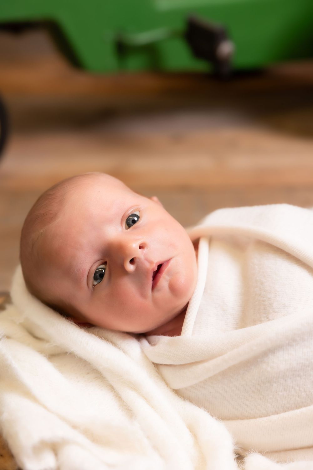 A baby wrapped in a soft white blanket looks up with bright eyes against a blurred background.