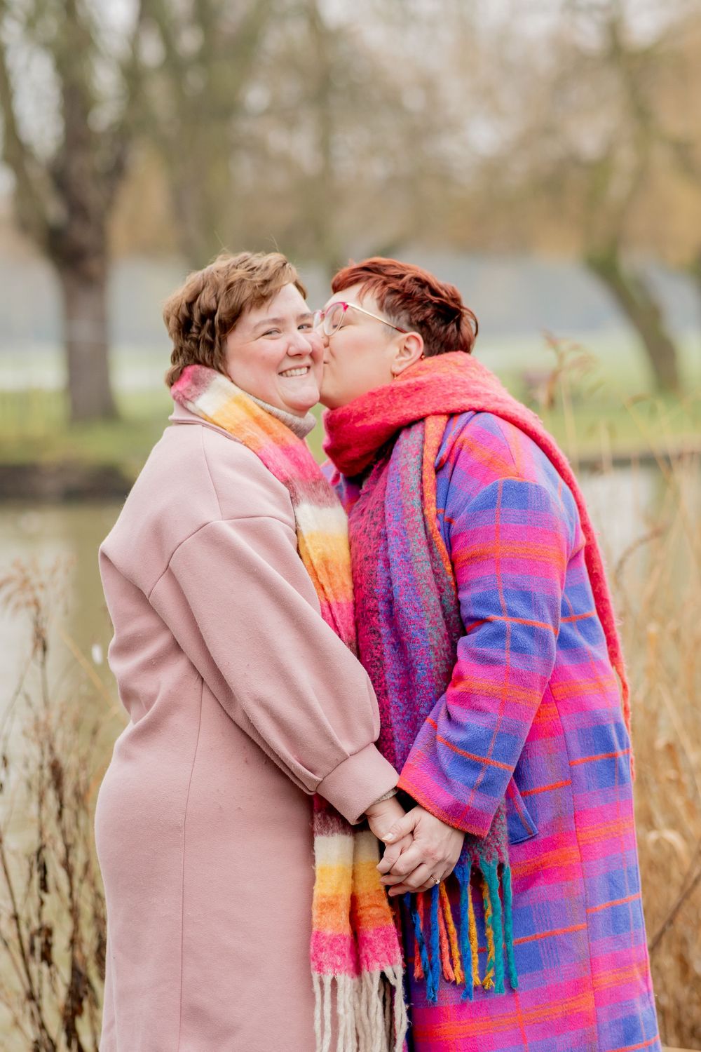 A loving couple in colorful winter coats sharing an intimate moment outdoors near a lake.