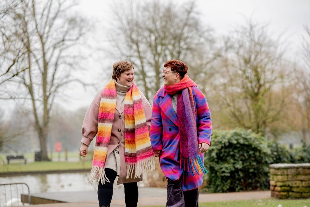 Two people in colorful winter coats walking and talking together along a canal path on a misty day.