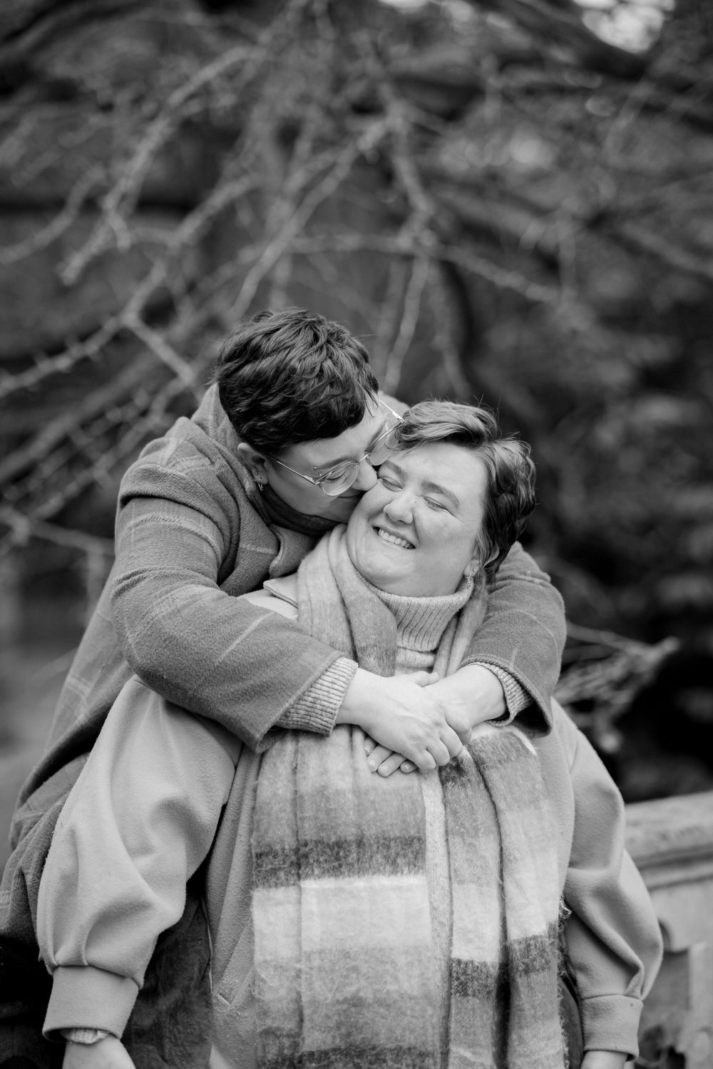 A black and white intimate portrait of two people sharing a tender embrace outdoors.