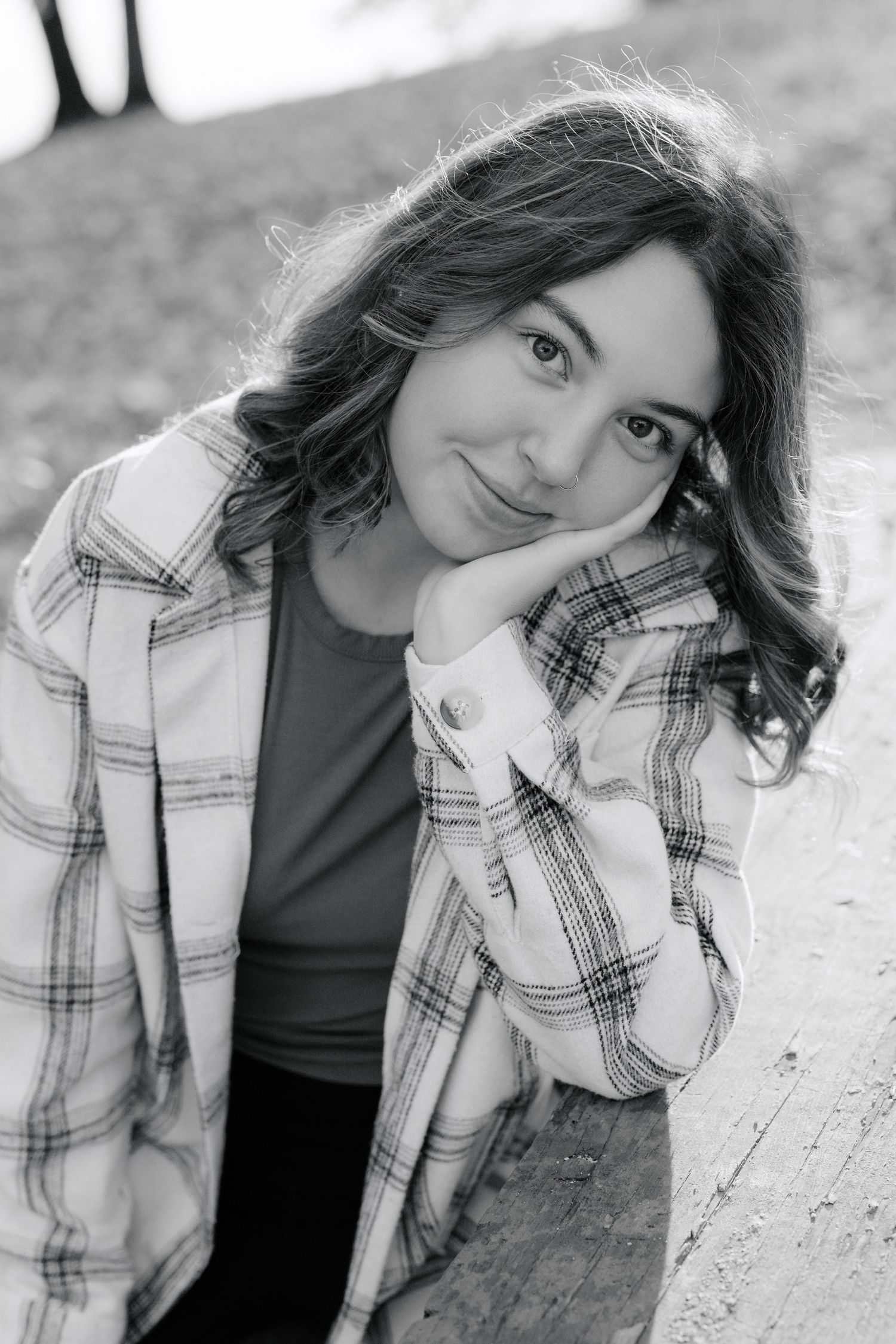 A black and white portrait of someone wearing a plaid jacket and resting their head on their hand.