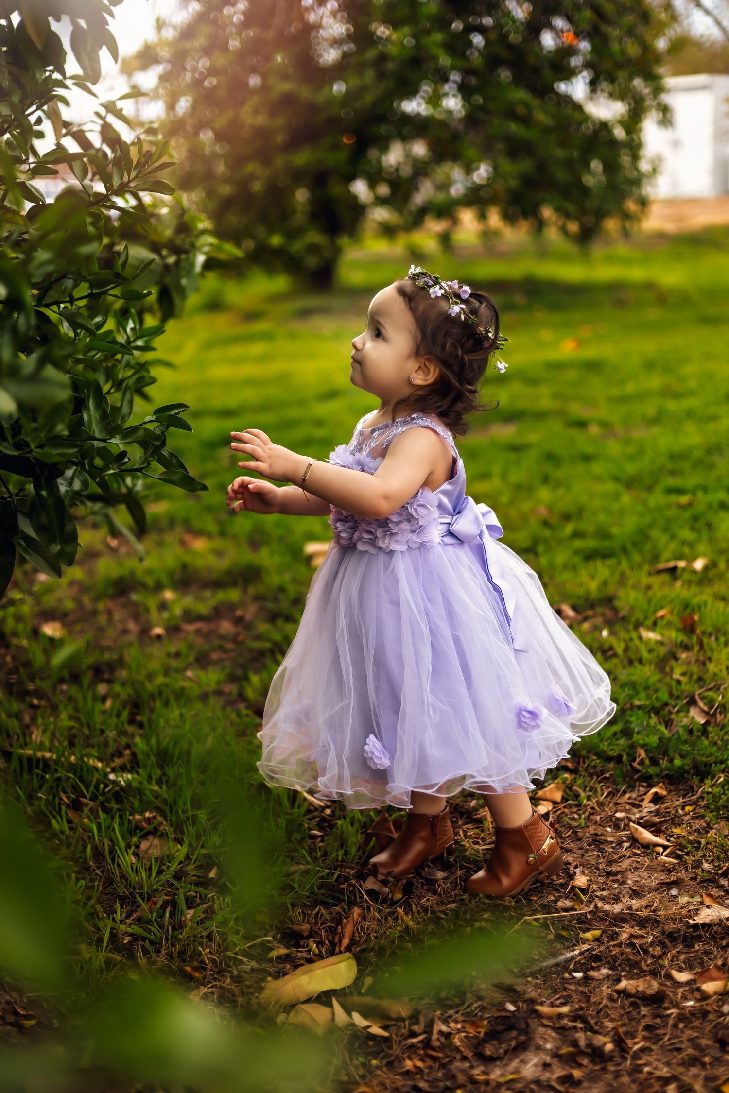 Young girl in purple tulle dress reaching for something in a garden for her first milestone photos in Glendale Arizona
