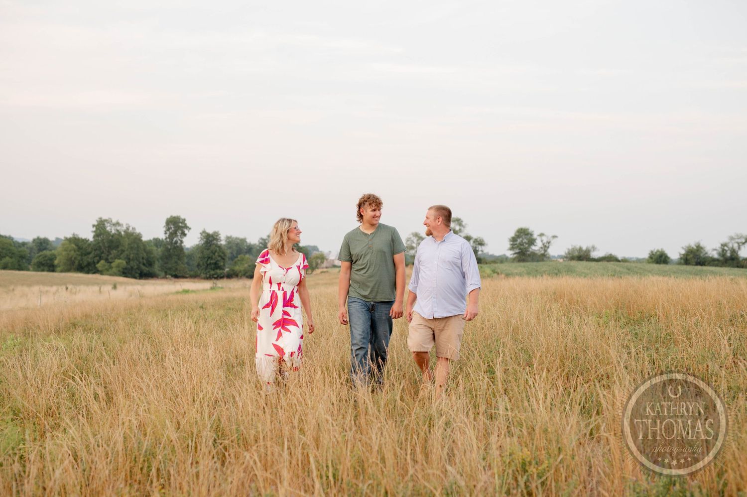 Three people walking together through tall grass in a field at sunset.