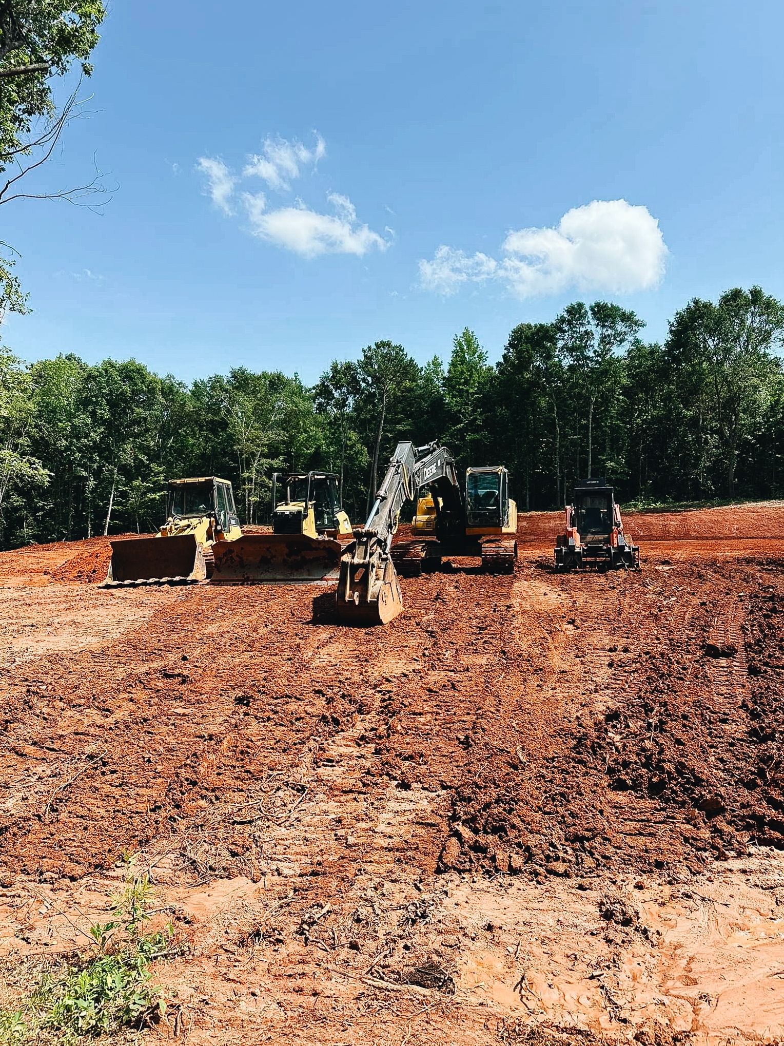 Construction equipment working on red clay dirt site with excavators and bulldozers.