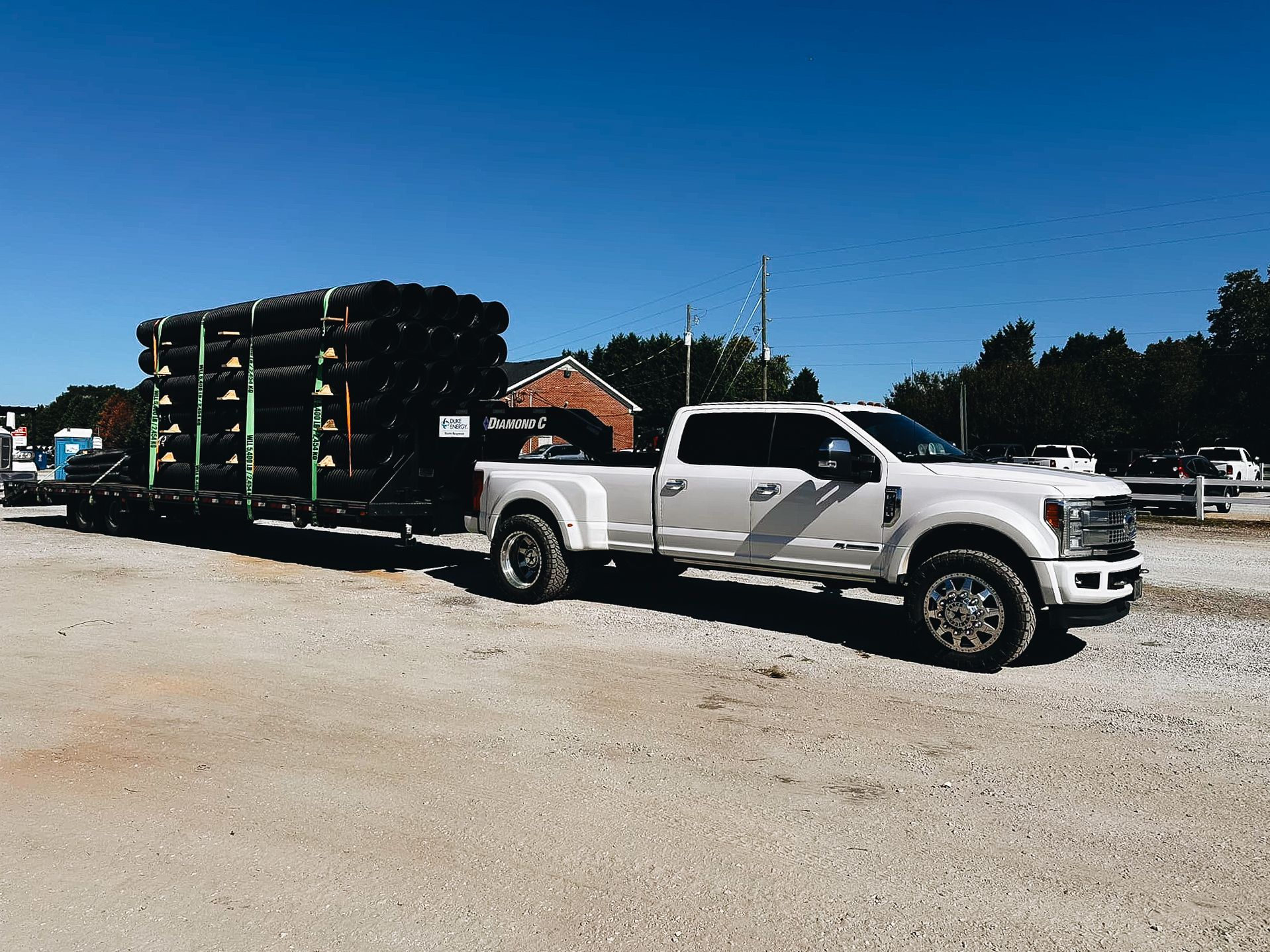 White Ford Super Duty pickup truck hauling a large trailer loaded with black tires on a dirt lot.