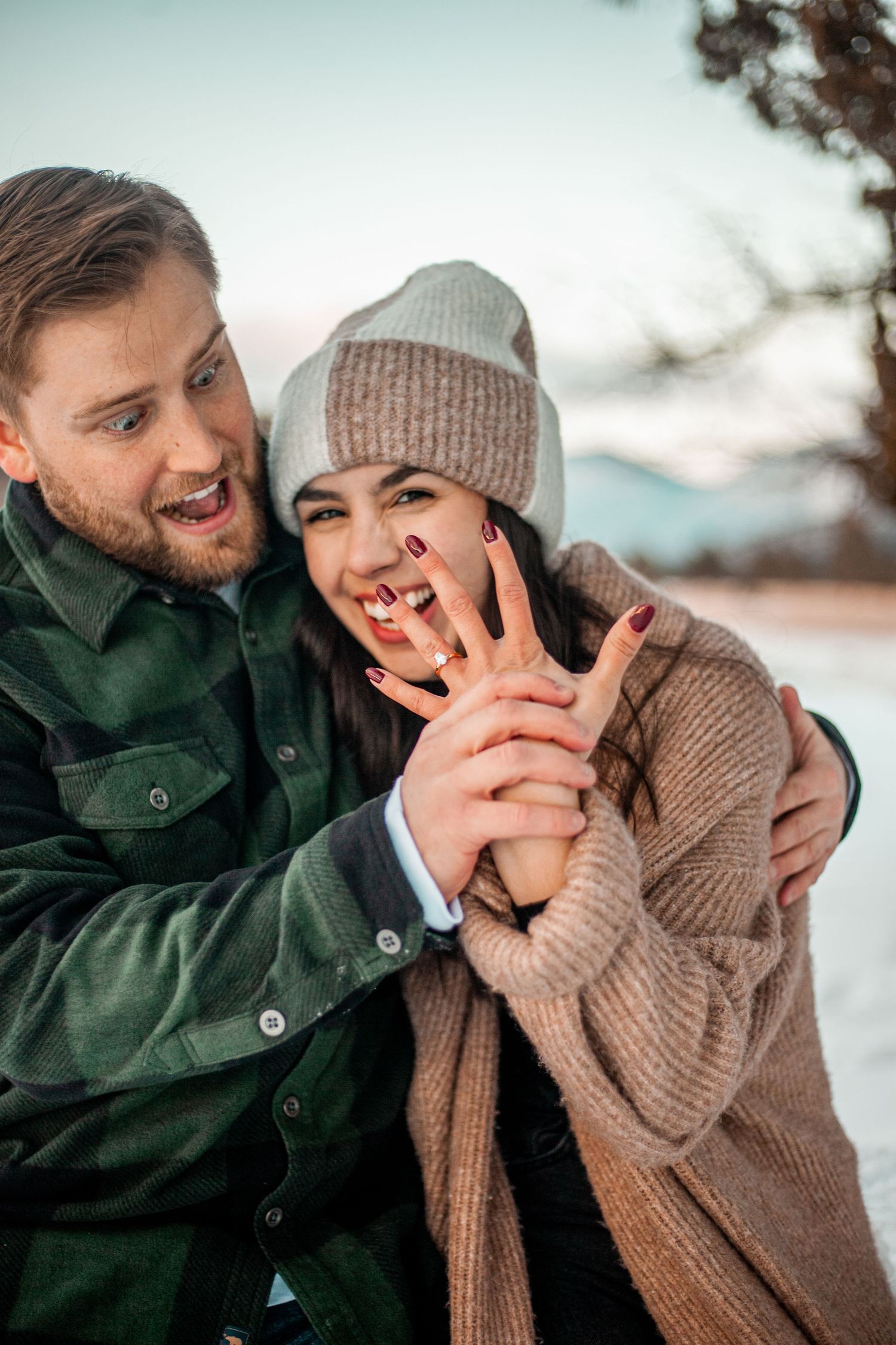 A playful winter couple moment outdoors with cozy knit sweaters and beanies against a snowy backdrop.