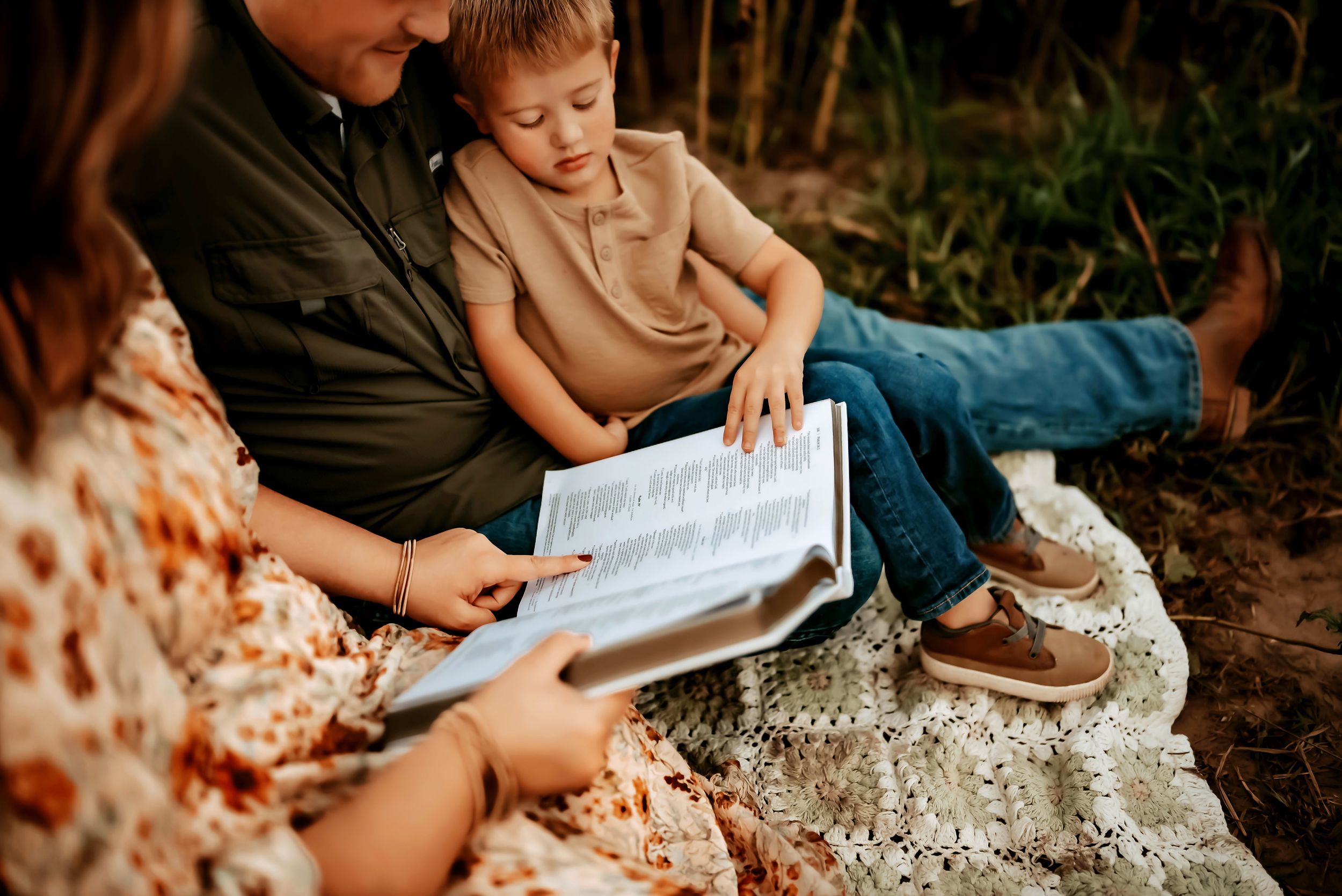 A parent and child sit outdoors reading a book together during a warm autumn afternoon.