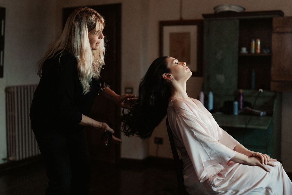 A hairstylist styles a client's hair in a moody, dimly lit salon interior.
