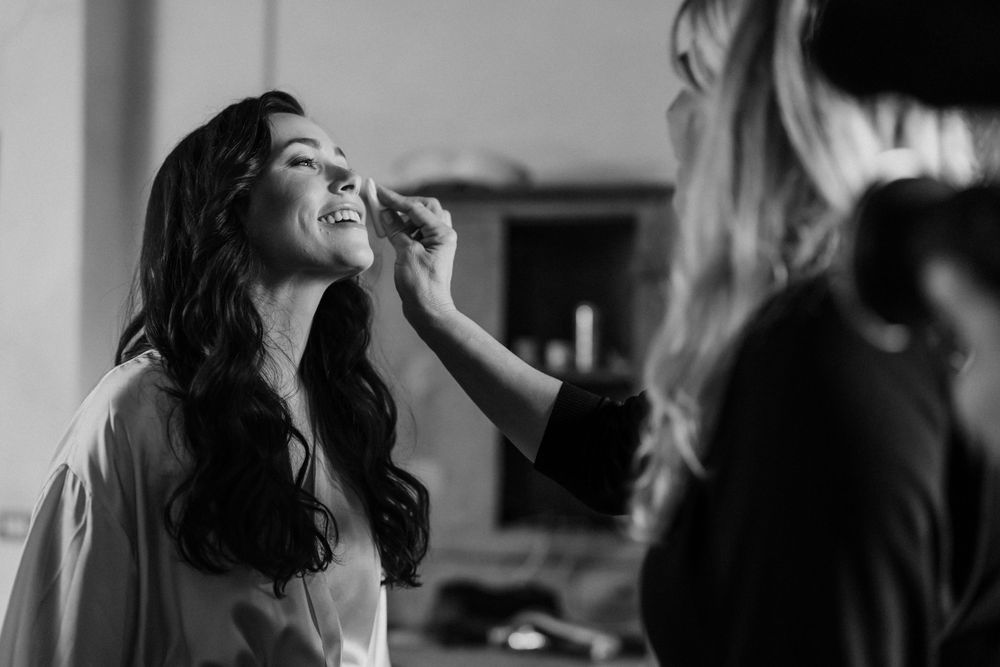 A black and white photo showing someone having makeup applied during wedding day preparations.