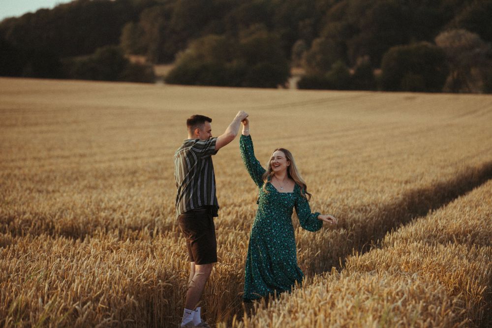 A couple dances together in a golden wheat field at sunset, sharing a joyful moment in nature.