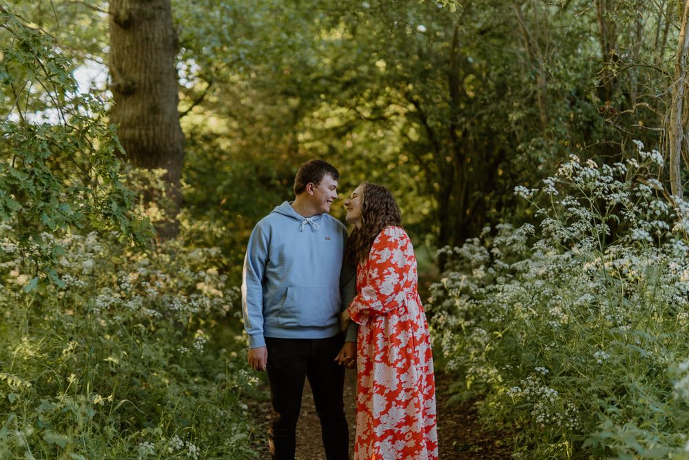 A couple stands together in a lush garden setting with white flowers blooming around them.