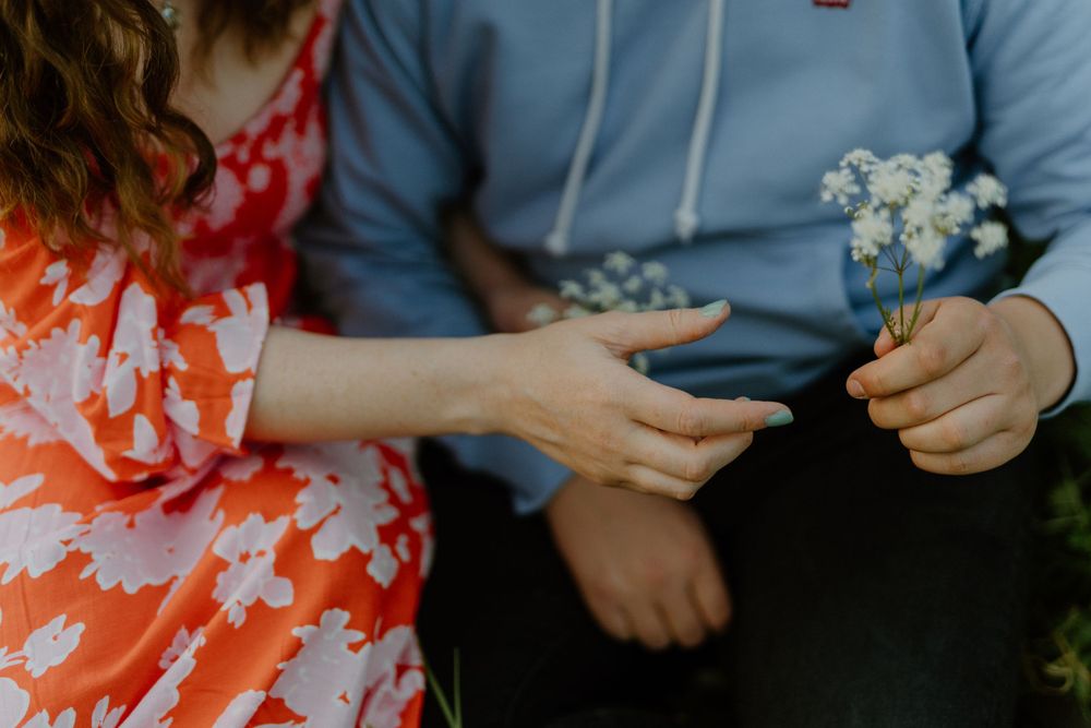 Hands exchange delicate white baby's breath flowers between two people wearing red and blue clothing.