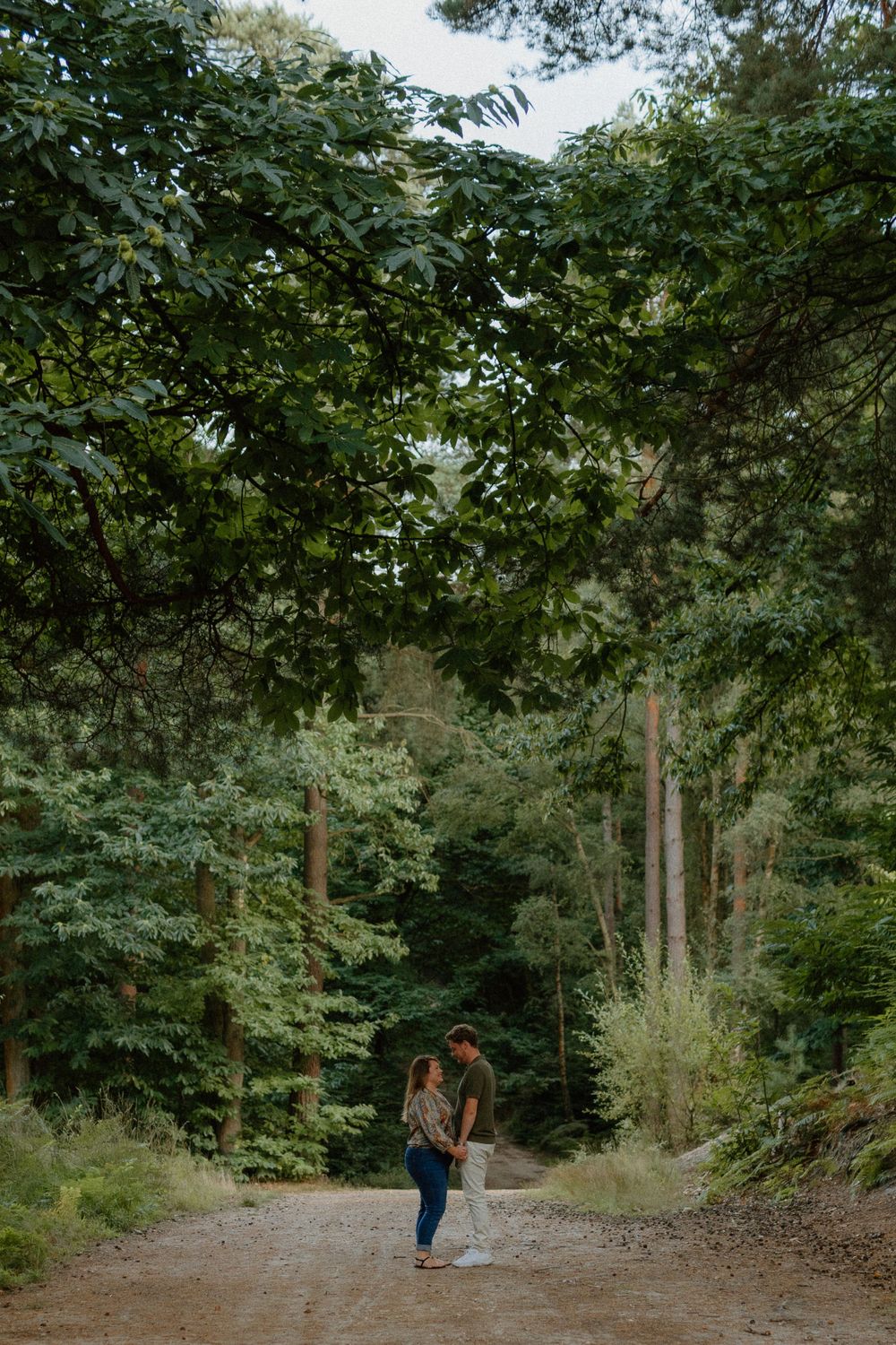 Two people stand together on a serene forest path surrounded by lush green trees and foliage.