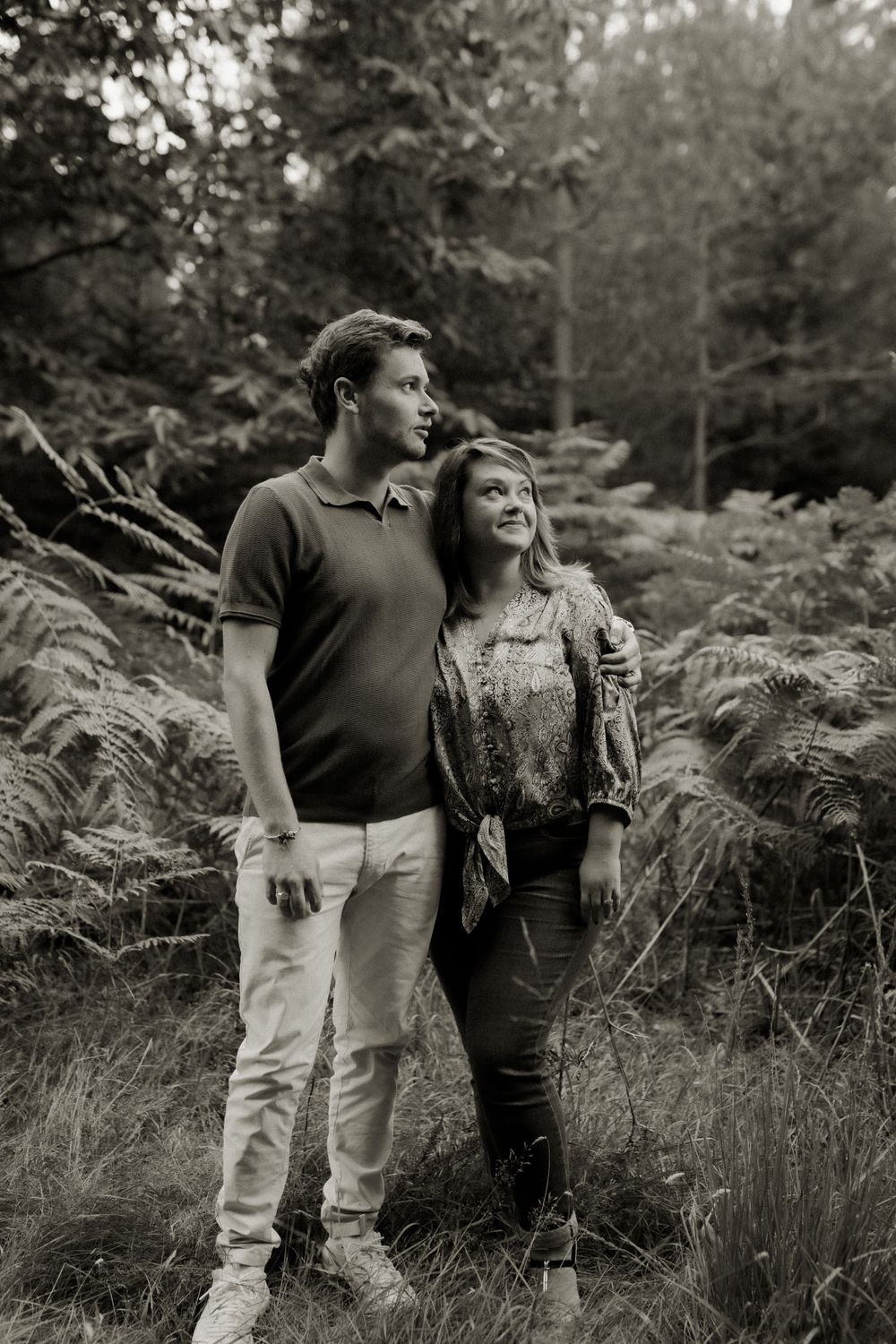 A romantic black and white photo of a couple standing among ferns in a wooded forest setting.