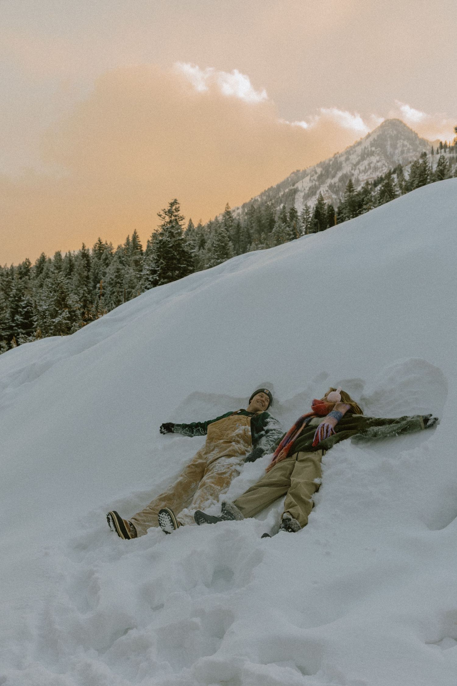 People laying in snow making snow angels against a mountain backdrop at sunset.