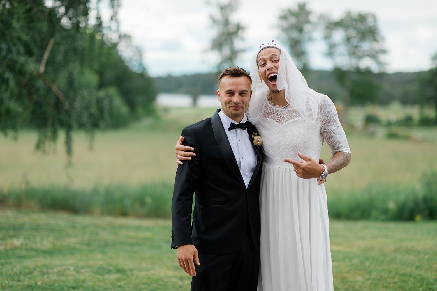 A couple in formal wedding attire dancing together on a grassy lawn during an outdoor celebration.