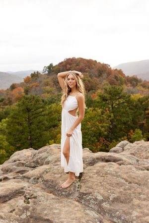 A white dress flows in the mountain breeze as someone poses gracefully on rocky terrain during autumn.