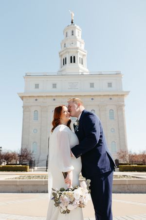 A romantic wedding couple shares tender moments outside a grand white Mormon temple with elegant architecture.