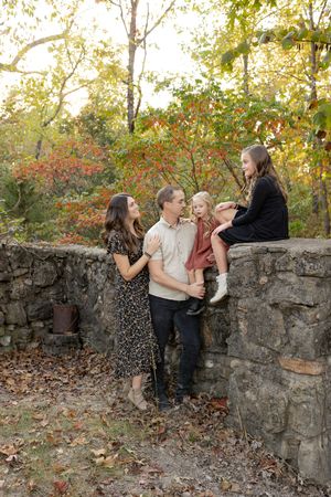 A group playfully throws autumn leaves against a rustic stone wall in a series of candid outdoor photos.