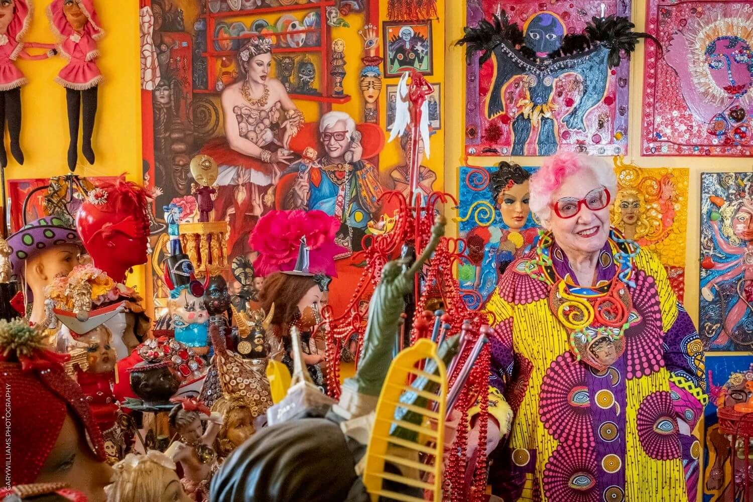 Vibrant art gallery interior with colorful pop art paintings and sculptures displayed against orange walls.