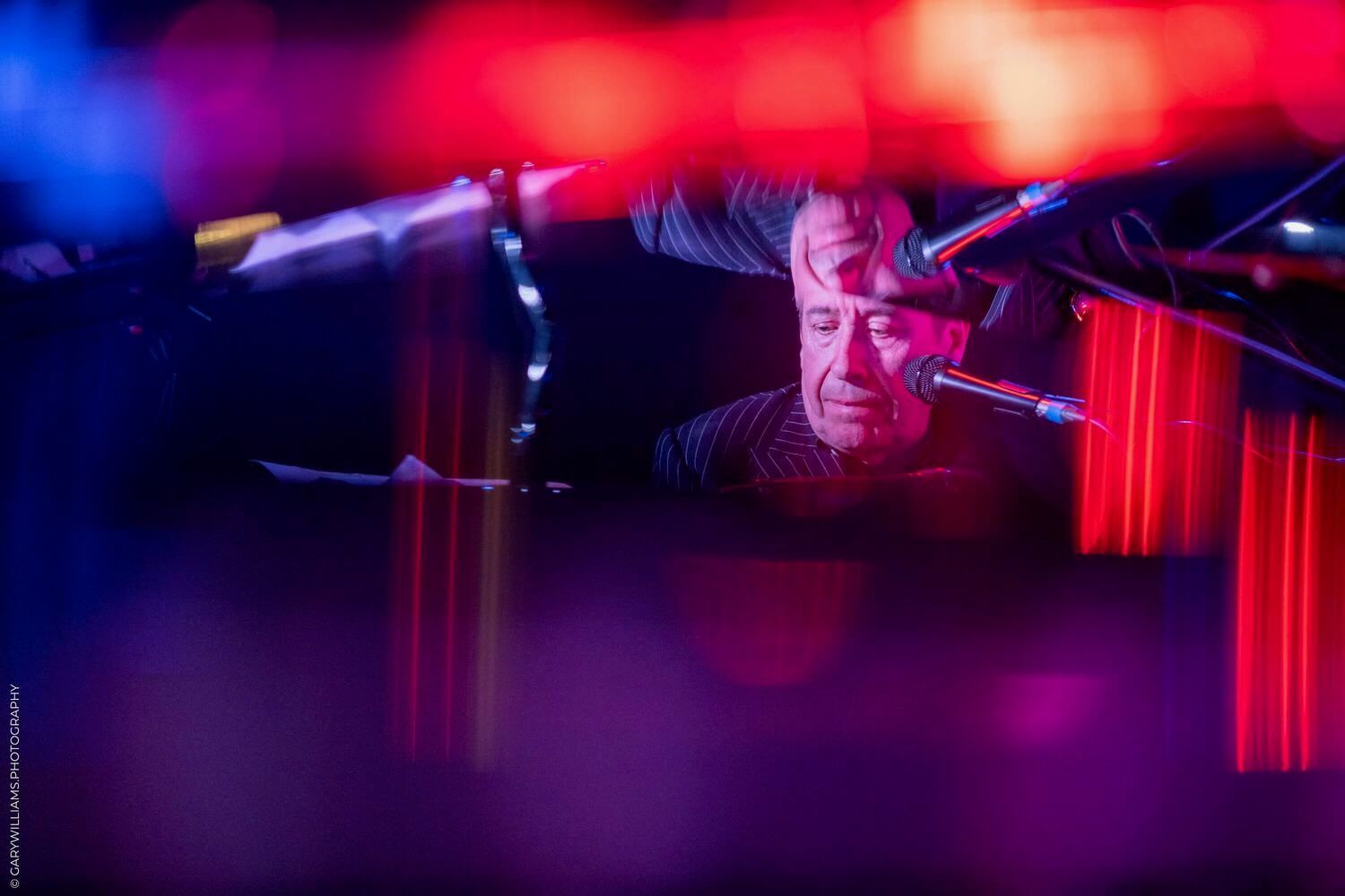 Colorful red and blue stage lighting illuminates a dark performance space with dramatic shadows and beams.